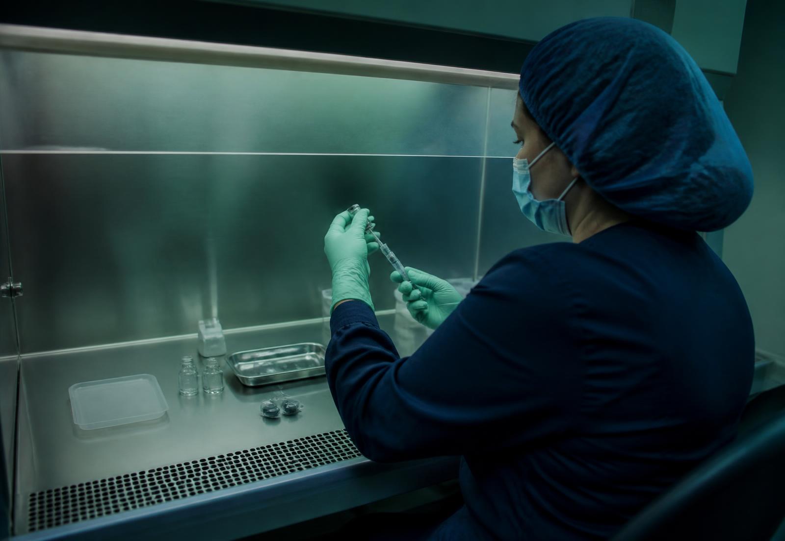 A pharmacist compounding medication under a sterile hood